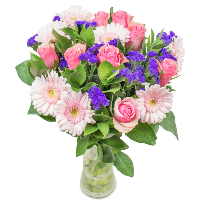 A striking, thoughtfully arranged bouquet fills a slender glass vase, its stems immersed in cool, clear water. Set against a pristine white backdrop, the ensemble features seven to nine elegant pink roses, their petals either tightly curled or just beginning to unfurl, capturing that fleeting moment of anticipation before full bloom. Around them, pale pink gerbera daisies with generous, radiating petals and luminous centres add softness and buoyancy. Clusters of bright, saturated purple statice interlace the arrangement, providing textural variety and vivid contrast. The base is composed of lush green foliage, reminiscent of Bromley Common's leafy streets and parks after rain, enhancing both the freshness and visual abundance. Each bloom is meticulously positioned, with light from a nearby window shimmering across the display. The transparent vase grounds the piece in quiet refinement, making this bouquet suitable for every thoughtful gift-whether for a birthday, anniversary, or simply as a vibrant accent on a local office desk. Together, the flowers convey a sense of joy, affection, and celebration, echoing the welcoming spirit of Bromley Common.